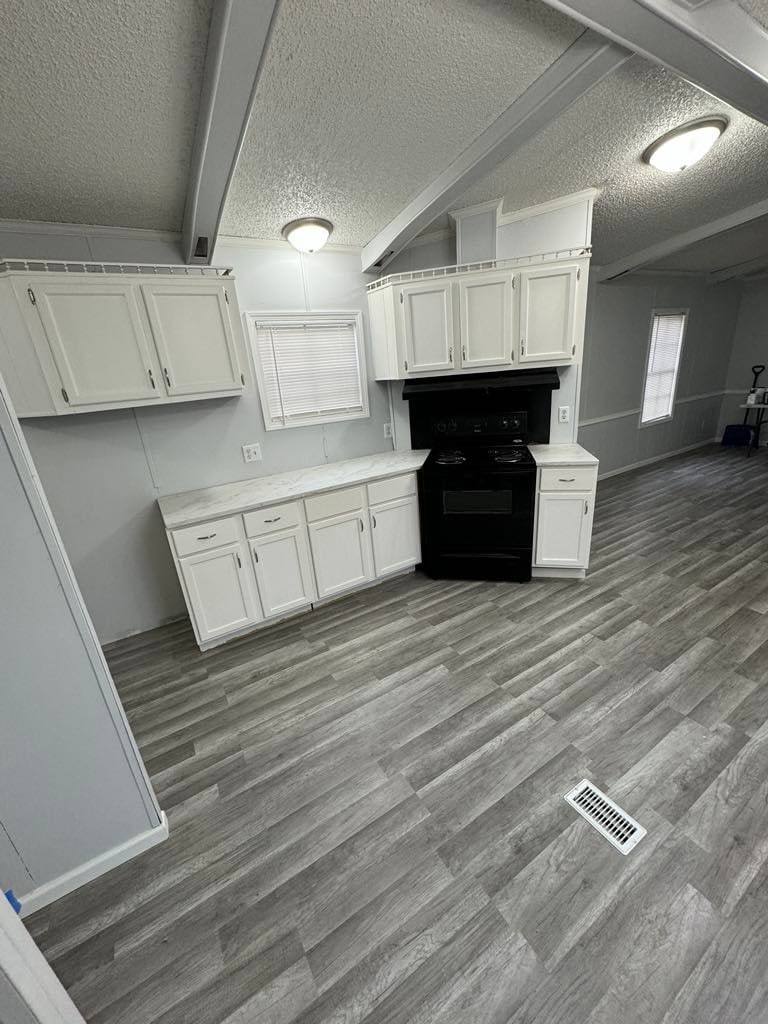 Kitchen with white upper and lower cabinets, a black range and a window