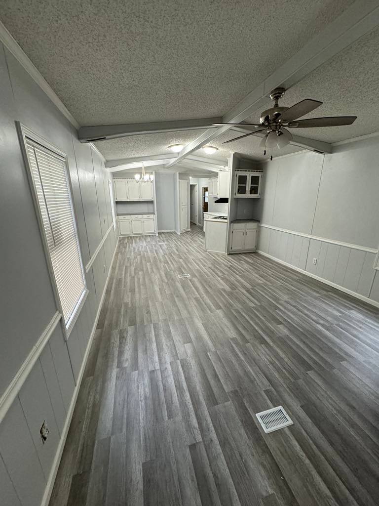 Long living room with a beamed ceiling, ceiling fan and a built-in hutch at the far end