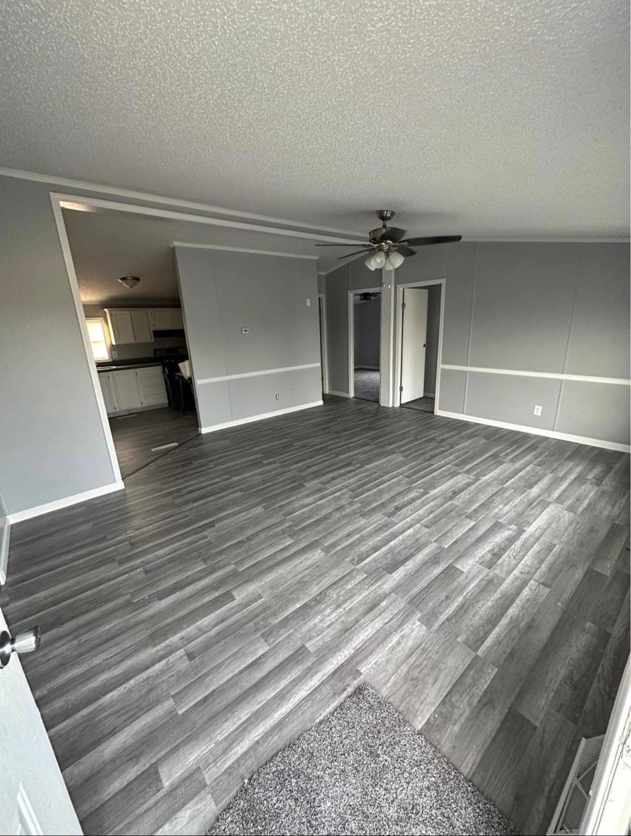 Open living room with gray plank flooring and a ceiling fan, looking through to the kitchen
